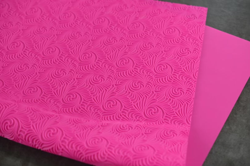 A textured pink mat with a swirl design rests on a dark surface. The mat is slightly folded on itself.