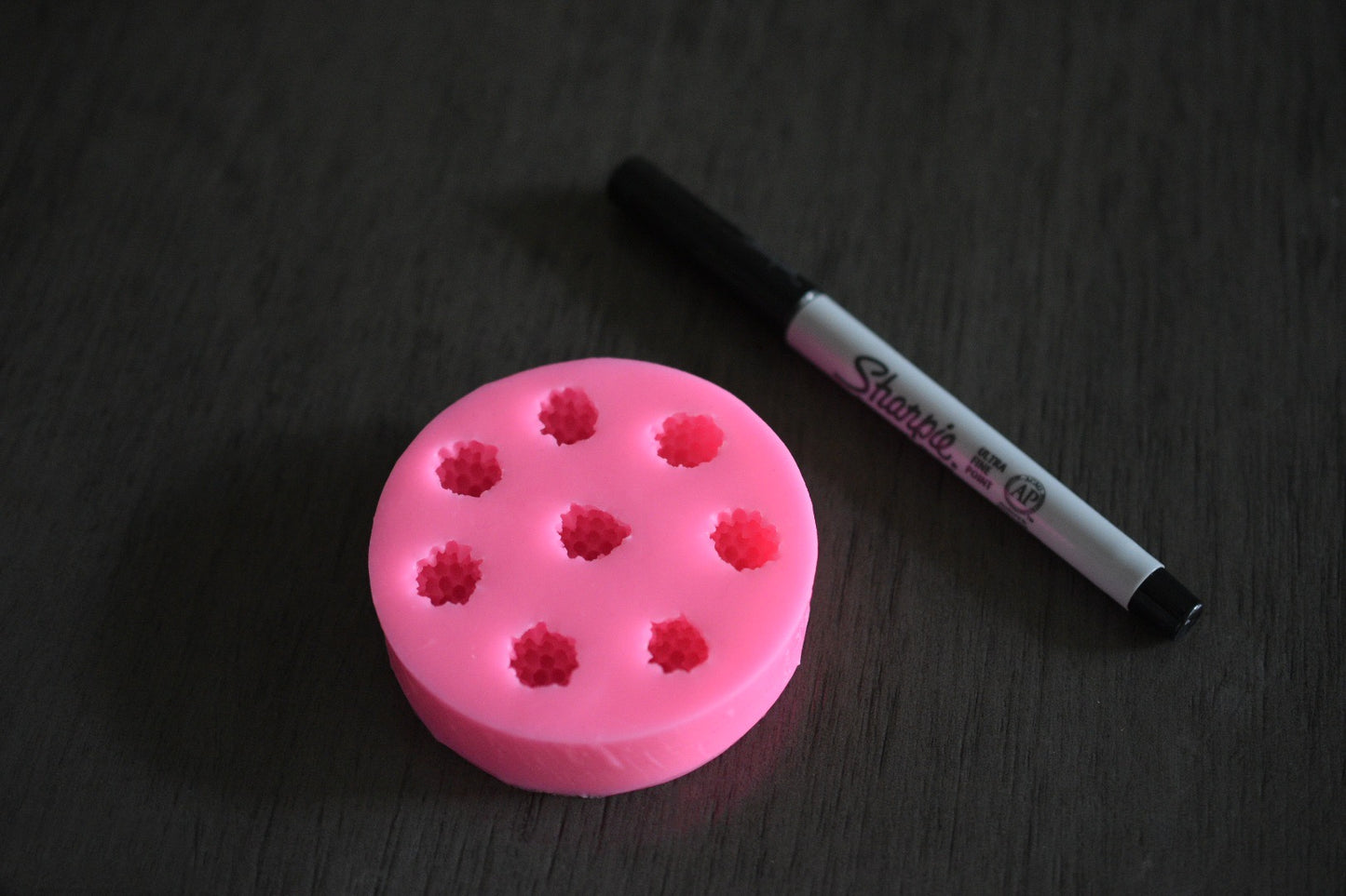 A top view of the black berry mold. It is next to a sharpie pen for size comparison. The sharpie is moderately longer than the mold in length. The soap mold is pink.