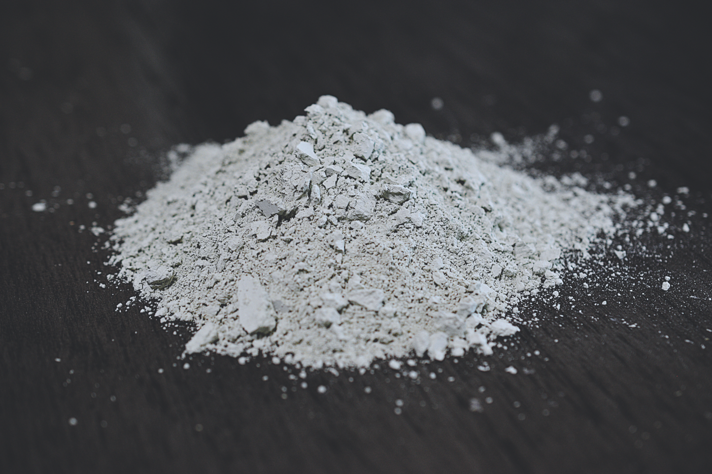 A close up view of a small pile of french green clay rests on a wooden surface. The clay is a very light green in color.