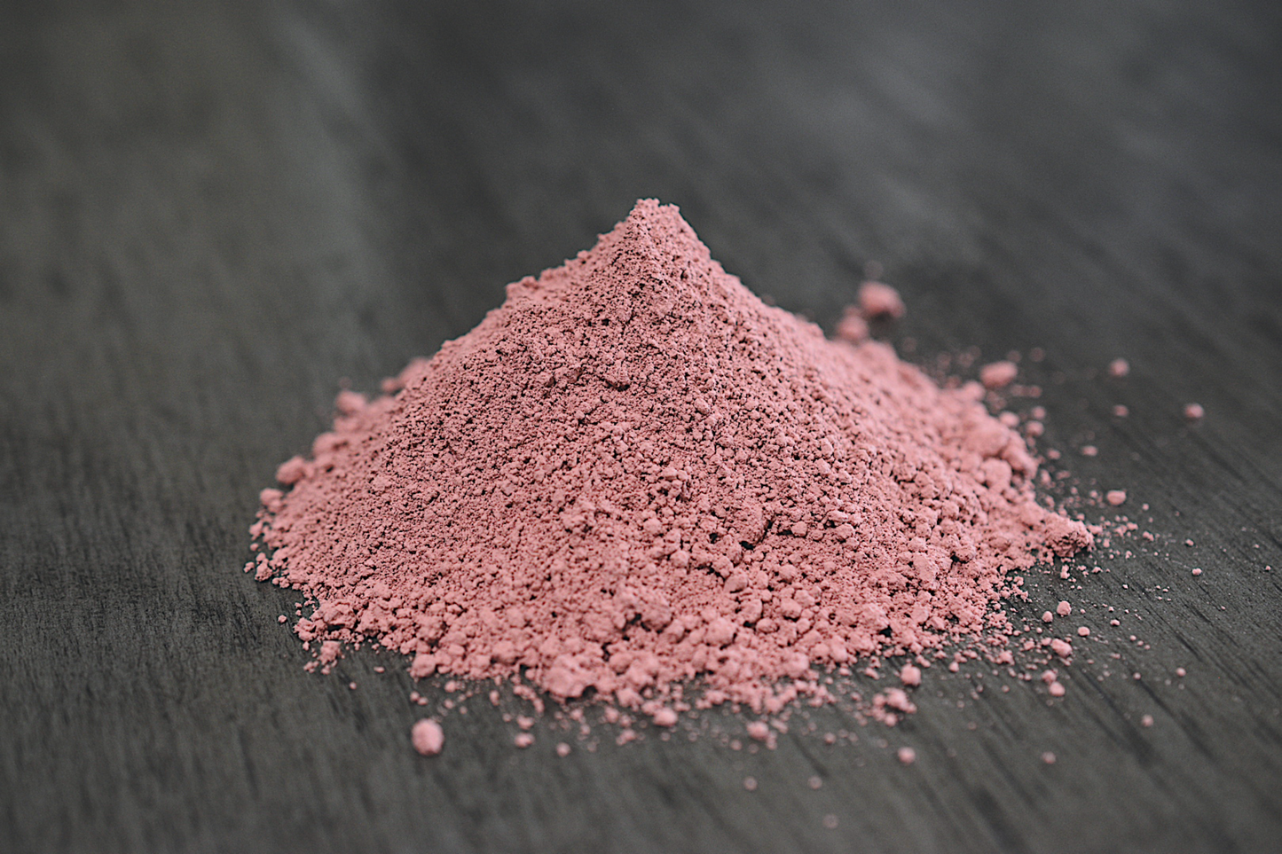 A close up view of a pile of rose clay rests on wooden surface. The clay is a light pink color.