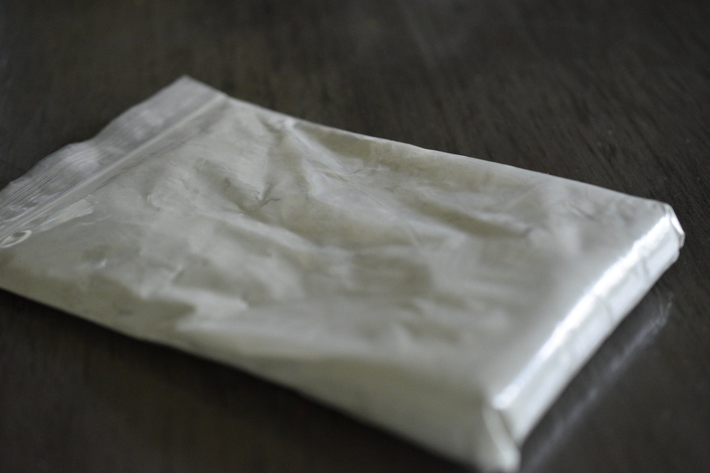 A plastic bag filled with french green clay rests on a wooden surface to show the packaged product. The clay is a very light green in color.