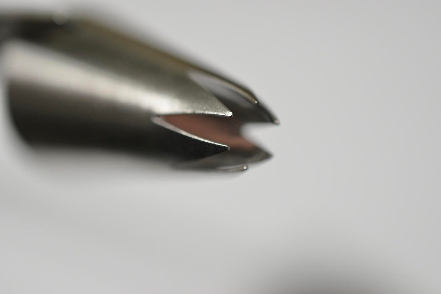 A metal piping tip with an open end shaped like an elongated star. The other end is open. The piping tip is on its side. It is against a white background.