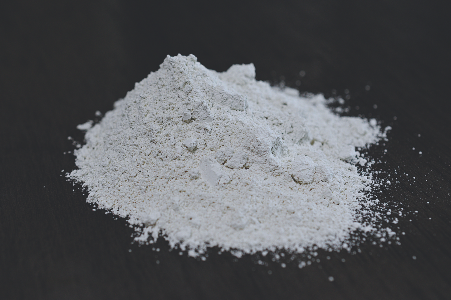 A pile of white kaolin clay rests on a wooden surface. The clay has a grey color.