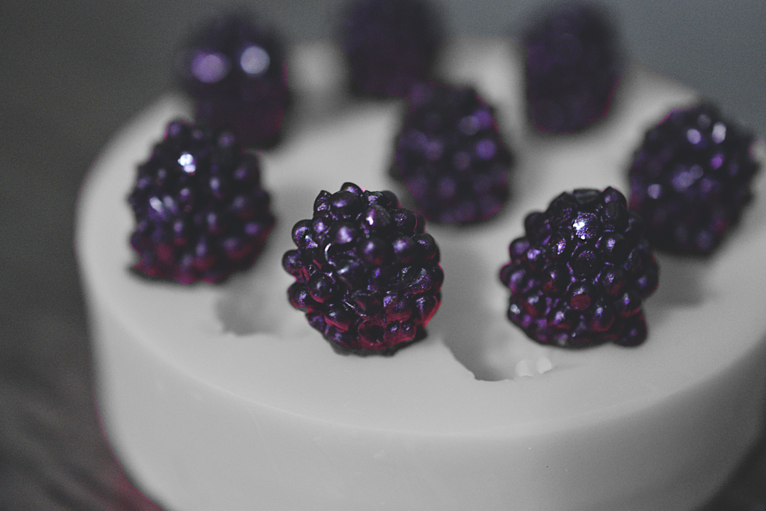 A close up view of the black berry mold, showing completed soap black berries. The soap blackberries have been colored a dark purple. The soap mold is grey.
