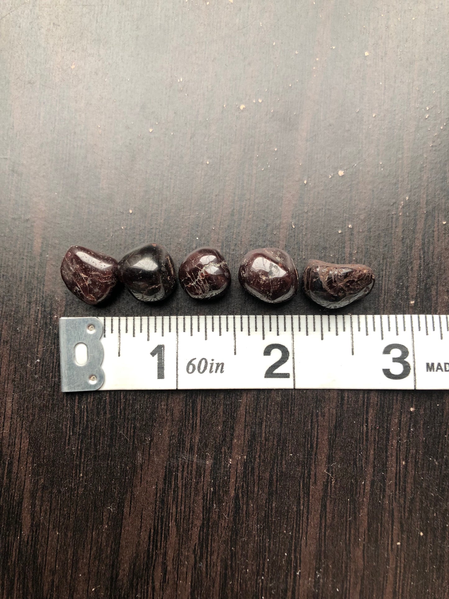 Five black garnet stones sit against a dark wood background. They are next to a white ruler showing each stone is approximately half an inch wide.