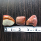 Three brown and red stones sit against a dark wood background. They are next to a white ruler showing each stone is approximately one inch wide.