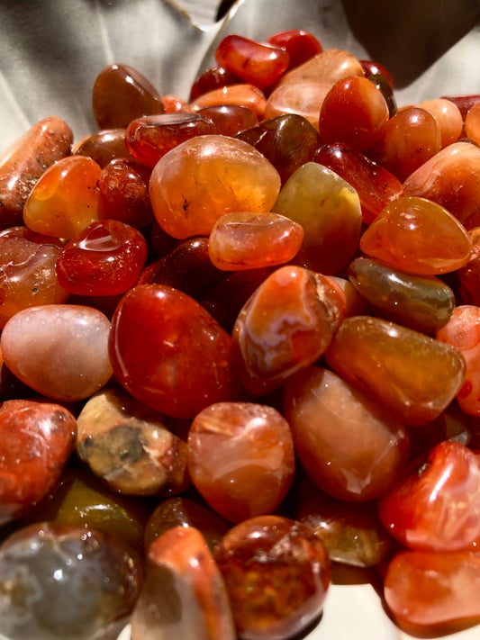 Close up view of carnelian stones. They are various hues of reds and oranges.