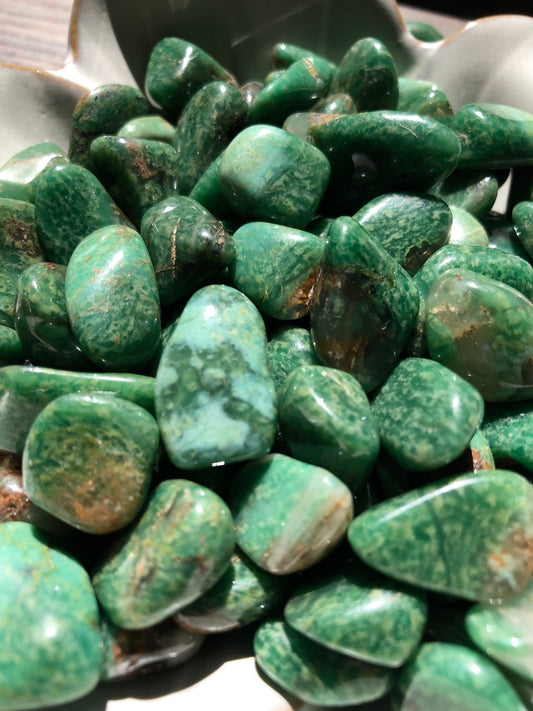A close up picture of green quartz stones. They are various hues of green with small amounts of brown.