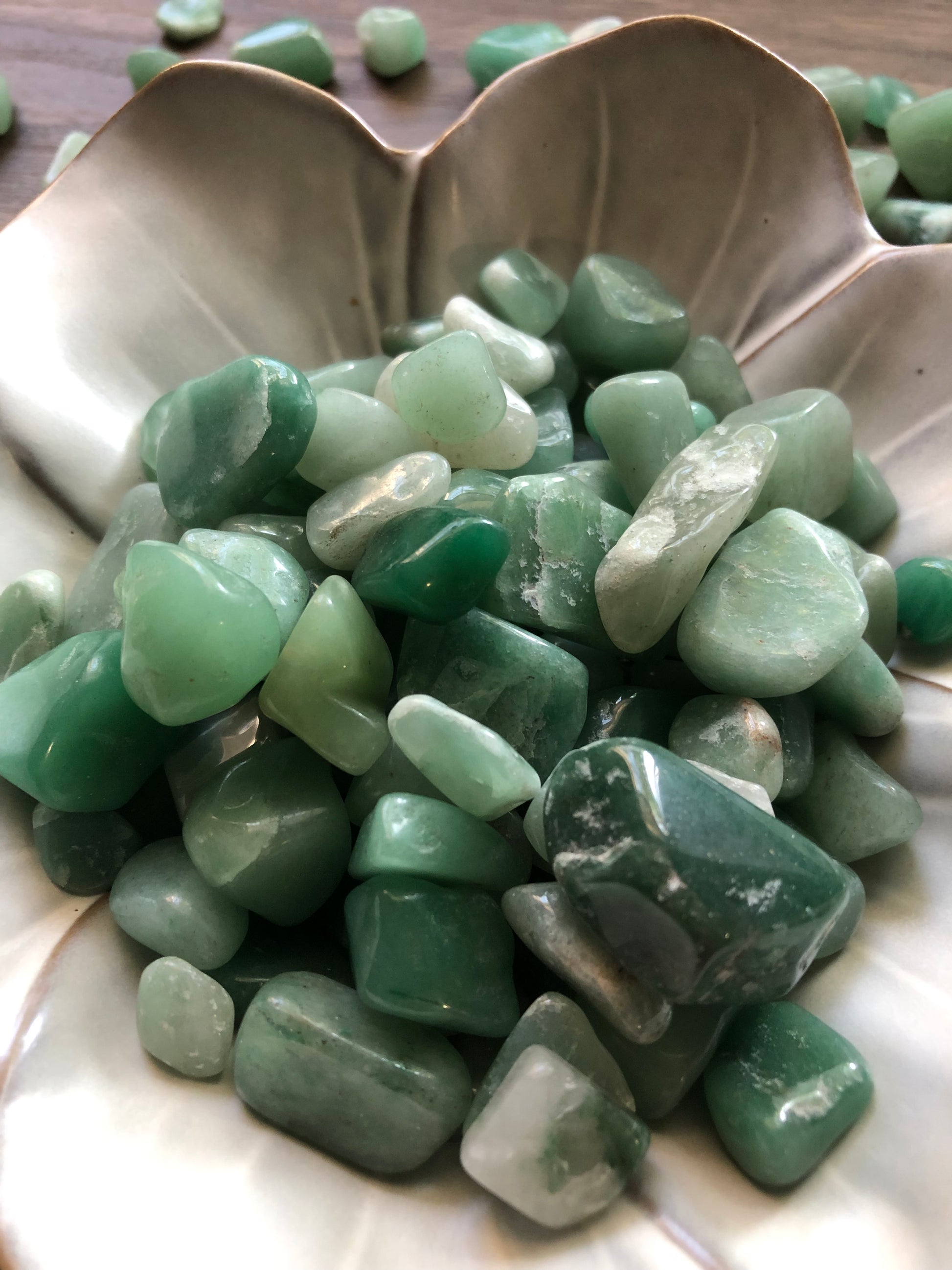 A close up picture of tumbled aventurine stones in a white bowl.