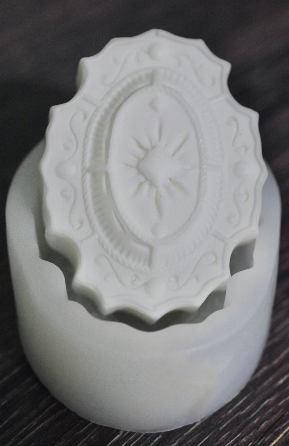 A white, oval soap bar with elegant and filigree design sits on a white mold.