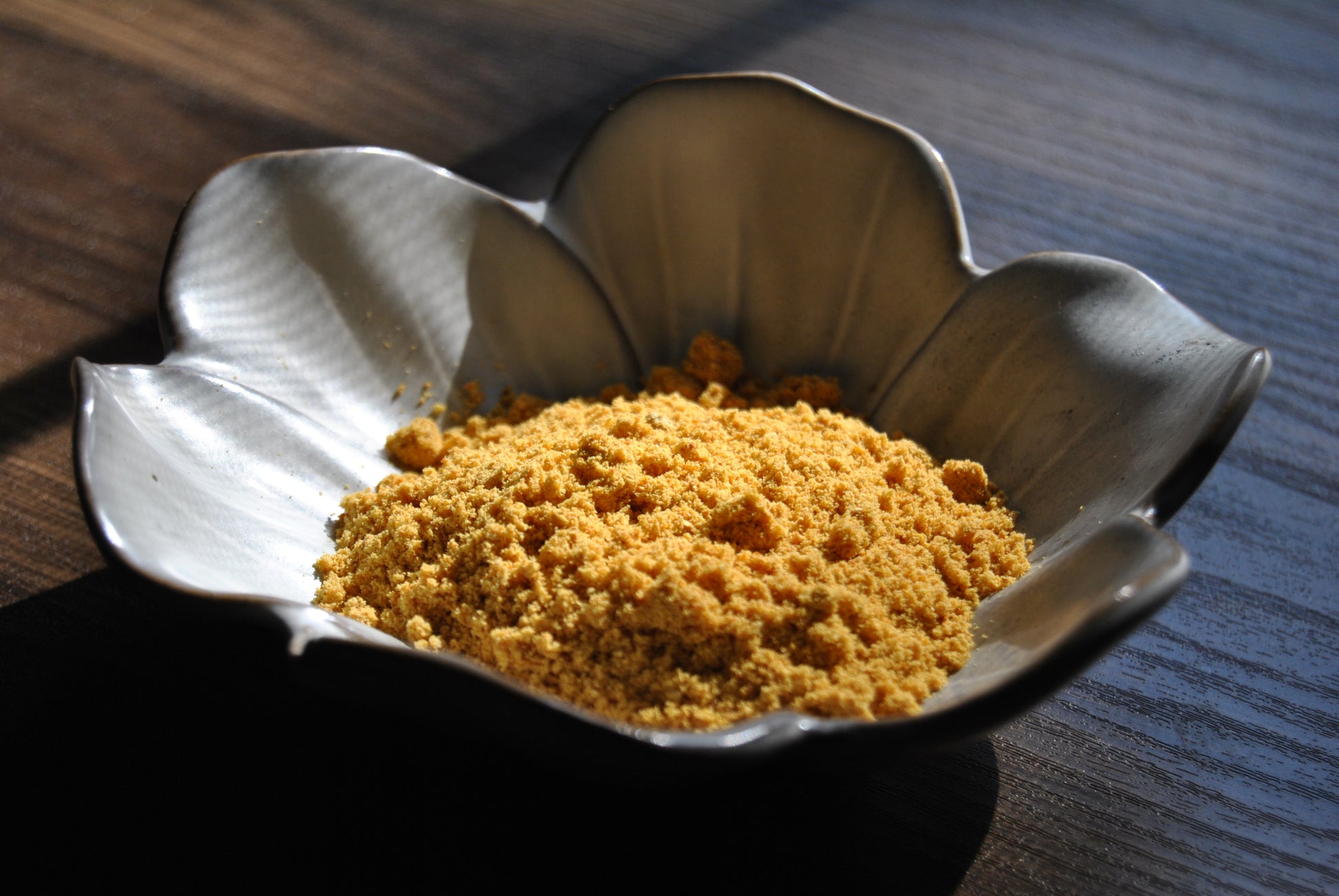 A close up view of a orange and yellow powder rests in a white, flower shaped dish on a wooden surface.
