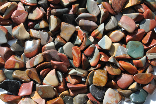 A top view of an assortment of tumbled desert jasper stones. The stones vary in hues of red, orange, blue and brown.