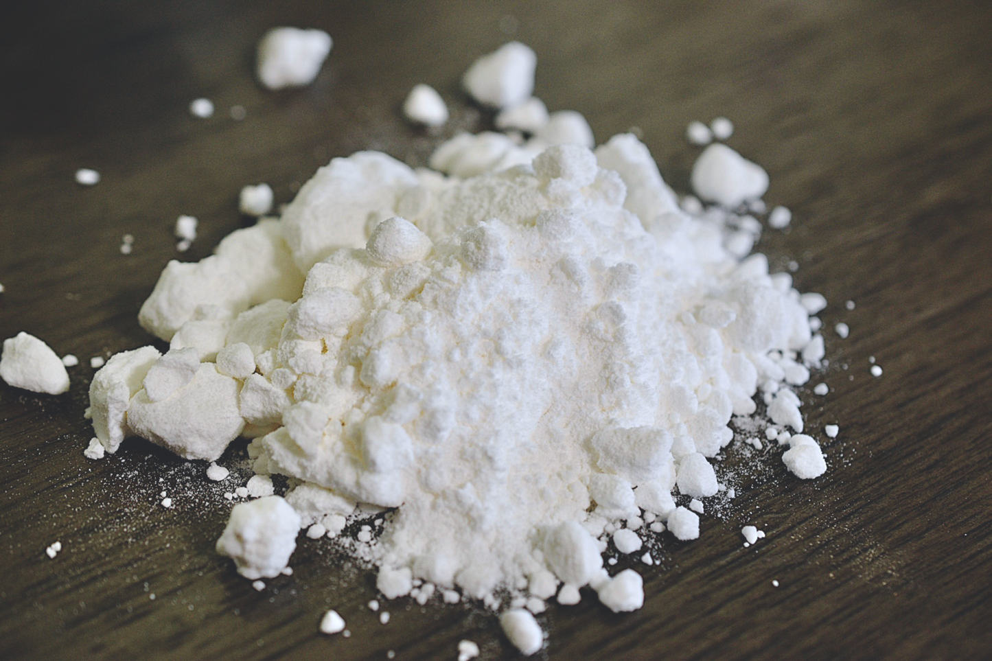 A close up view of the white and silky coconut milk powder rests on a wooden surface. Small clumps of powder are in the background of the photo.