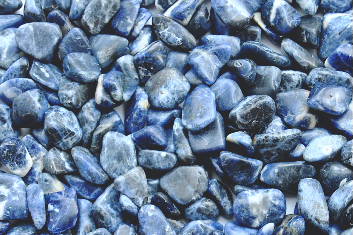 A top down view of an assortment of sodalite stones. The stones are various hues of blue with swirls of white on them.