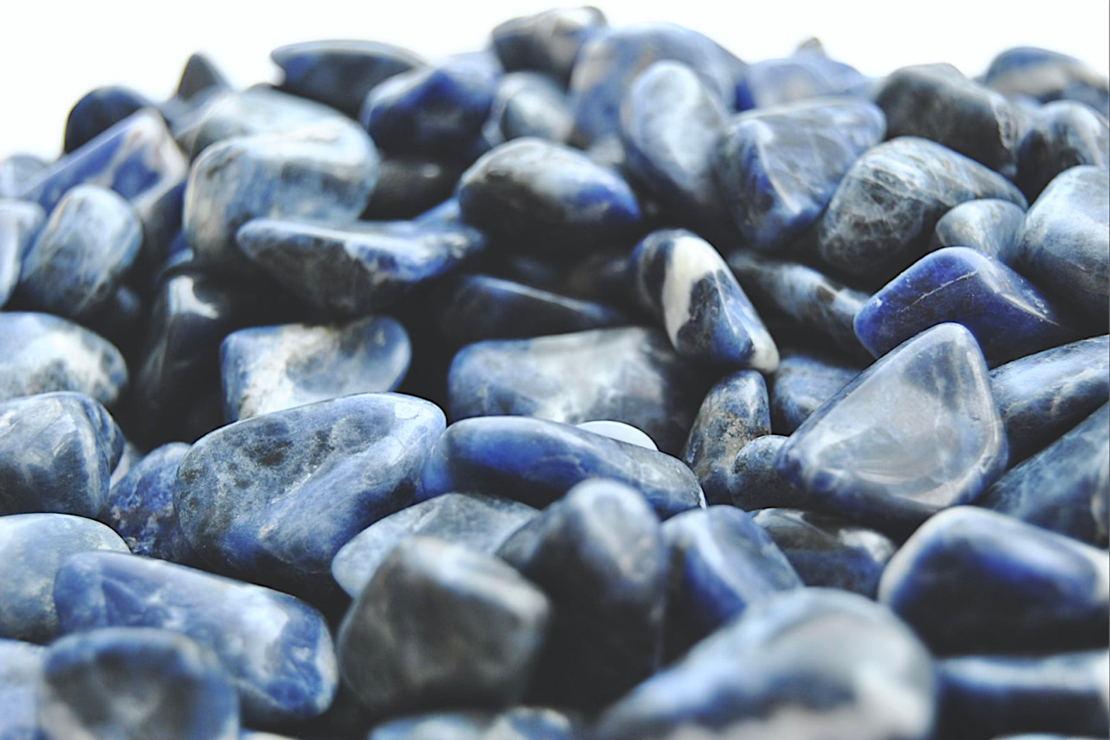 A close up view of an assortment of sodalite stones. The stones are various hues of blue with swirls of white on them.