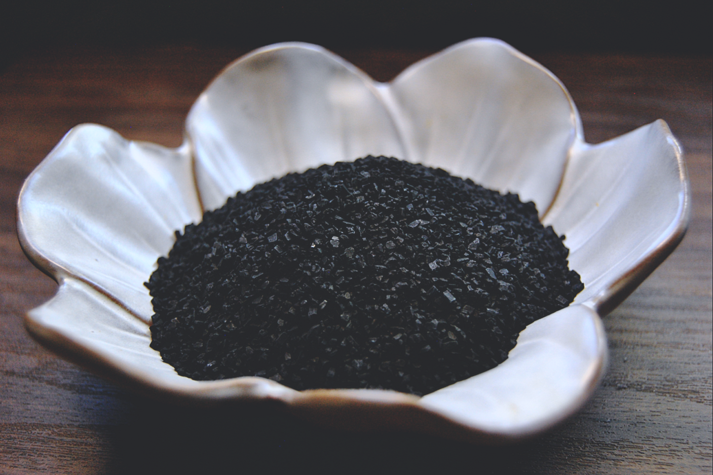 A photo of the black hawaiian sea salt in a small, white, flower shaped dish.