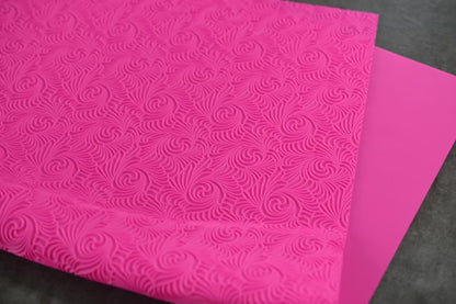 A textured pink mat with a swirl design rests on a dark surface. The mat is slightly folded on itself.