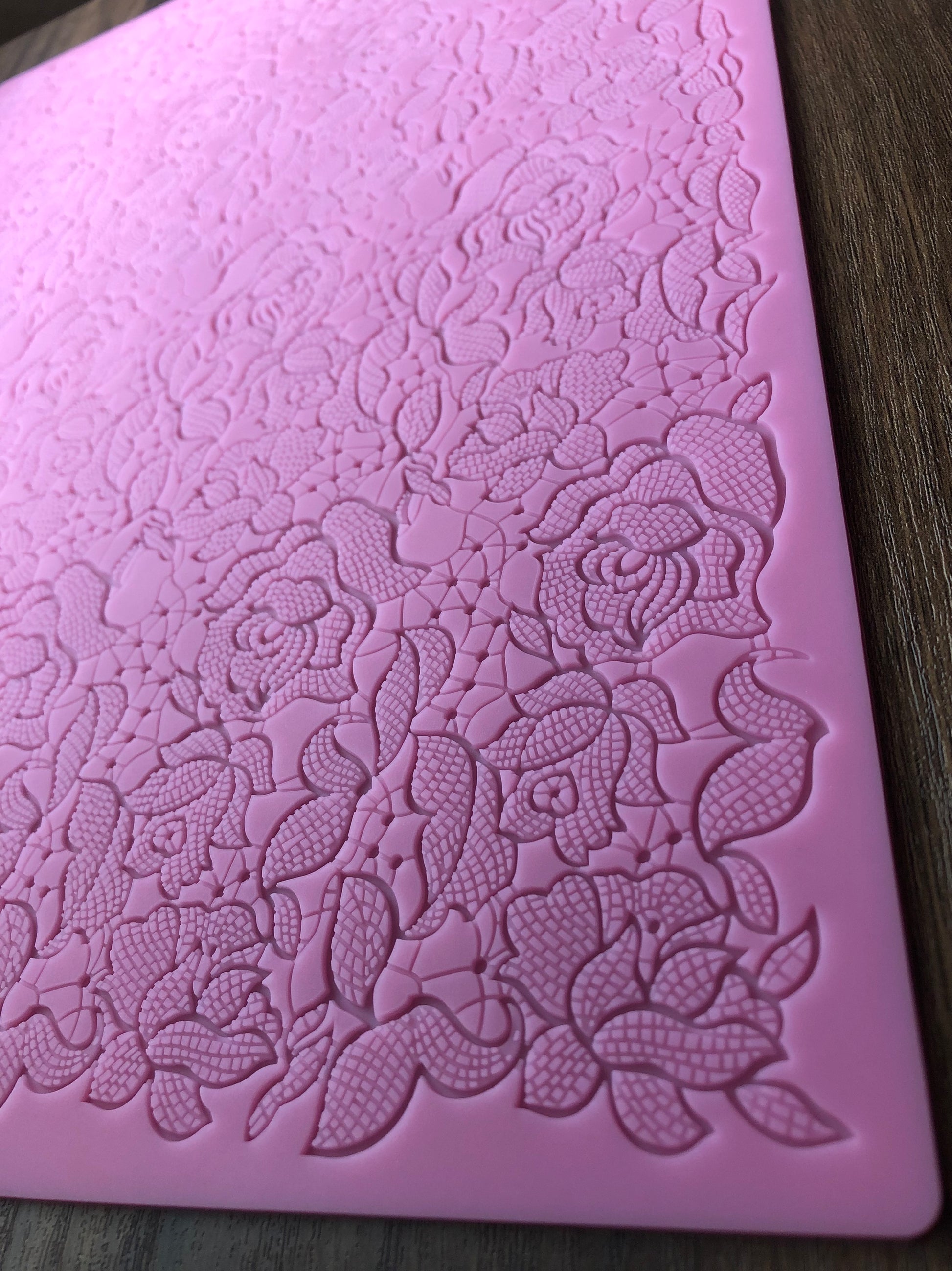 A close up view of a corner of the textured pink floral design mat on a wooden surface.