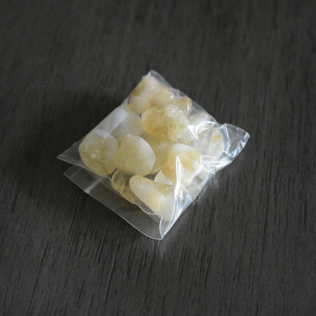 A packaged set of citrine stones in a plastic bag rests on a wooden surface. The stones are clear with hints of brown and white swirls on them.