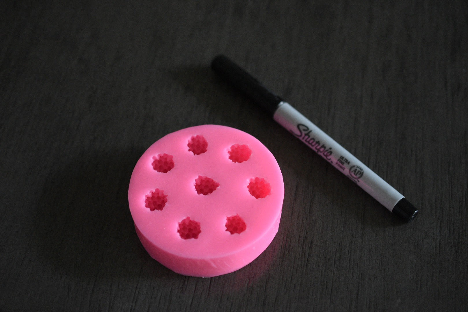 A top view of the black berry mold. It is next to a sharpie pen for size comparison. The sharpie is moderately longer than the mold in length. The soap mold is pink.