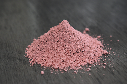 A close up view of a pile of rose clay rests on wooden surface. The clay is a light pink color.