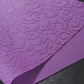 A textured purple mat with a floral filigree design rests on a dark surface. The mat is slightly folded on itself.