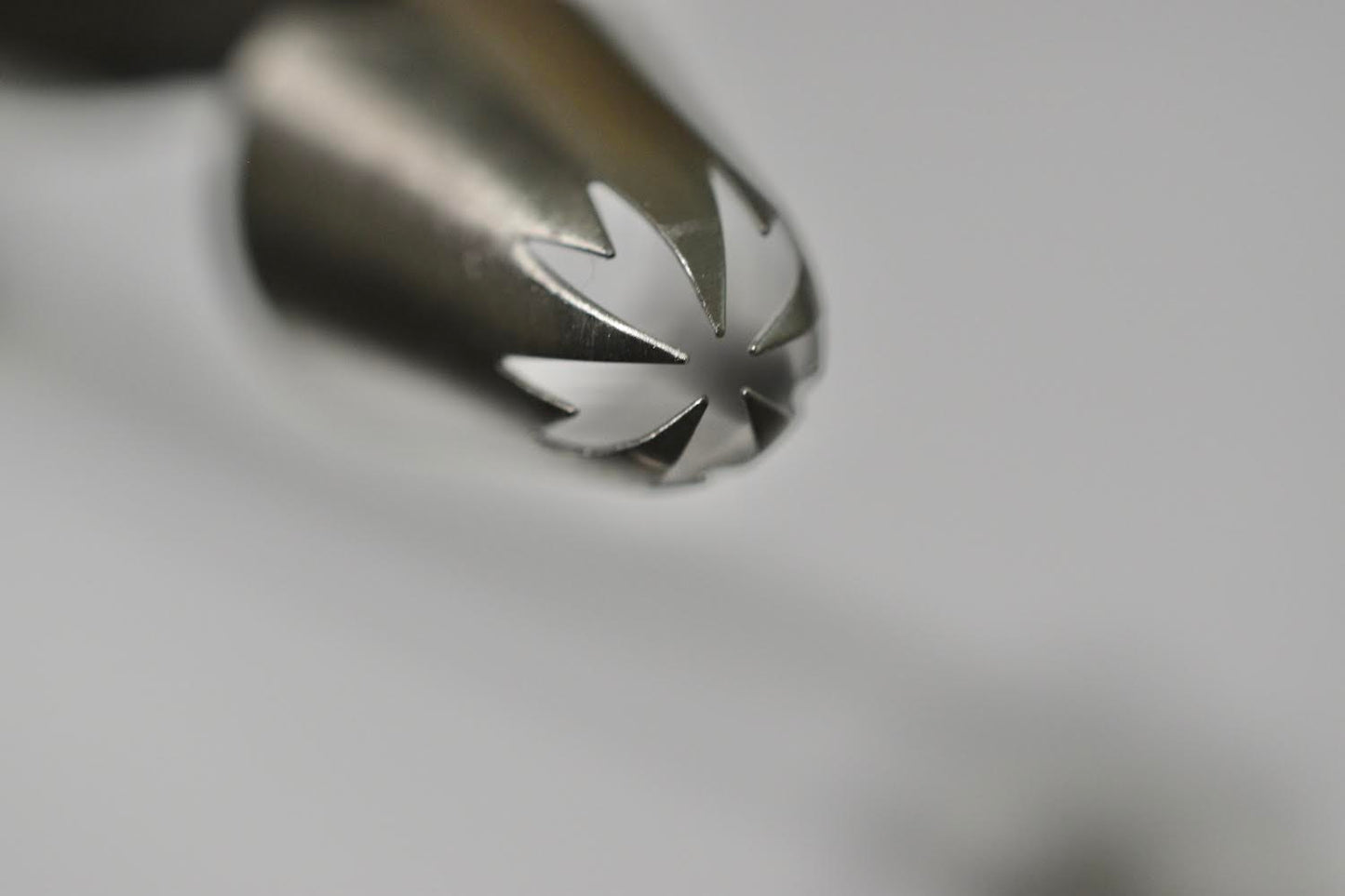 A metal piping tip with a jagged star opening on one end. The other end is open. The piping tip is on its side. It is against a white background.
