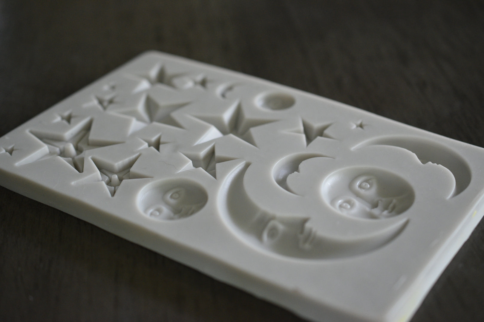 A close up view of the celestial mold. The mold shows small moons and stars, some with stoic faces on them. The mold is grey.