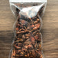 A small plastic bag filled with star anise pieces to show the packaged product rests on a wooden surface. Most pieces are missing petals or are chipped. The star anise pieces are dark brown in color.