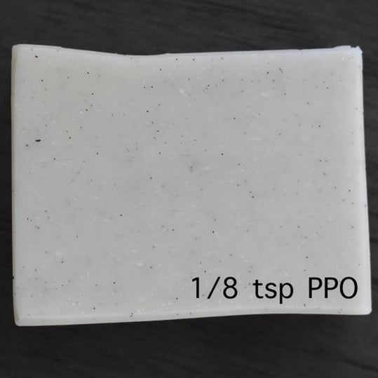 A close up view of a square bar of white soap with vanilla powder in it. It has slight dark speckles throughout the bar. There is text that shows 1/8 teaspoon pound per oils.