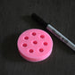 A top view of the blueberry mold on a wooden surface. A sharpie pen is next to it for size comparison. The sharpie pen is moderately longer than the mold. The mold is pink.