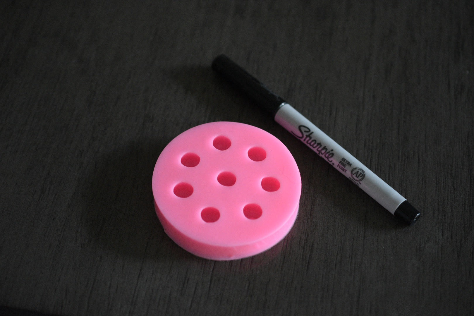 A top view of the blueberry mold on a wooden surface. A sharpie pen is next to it for size comparison. The sharpie pen is moderately longer than the mold. The mold is pink.