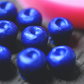 A close up of blueberries made from soap on a wooden surface. The blueberries have been colored blue. In the background is the blueberry mold. The mold is pink.