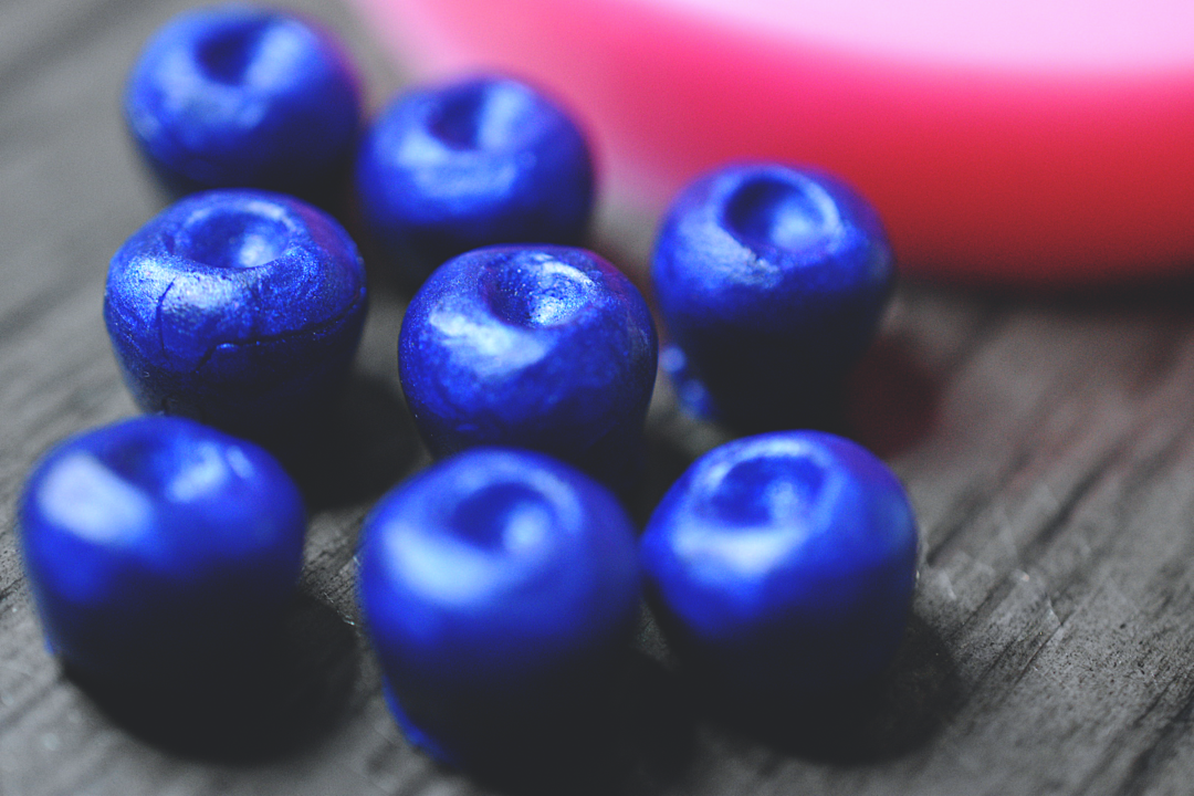 A close up of blueberries made from soap on a wooden surface. The blueberries have been colored blue. In the background is the blueberry mold. The mold is pink.