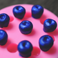 A close up view of blueberries made from soap sitting on the blueberry mold. The soap blueberries have been colored blue. The mold is pink.